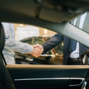 Buyer of car shaking hands with seller in auto dealership, view from interior of car.